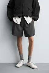 Bermuda de corte relajado color gris oscuro jaspeado, con cintura elástica negra ajustable mediante cordón negro. Presenta bolsillos frontales y bolsillos traseros de vivo.