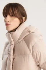 Campera puffer corta color beige con capucha desmontable, cierre frontal con cremallera y botones a presión, y cordón ajustable en el ruedo. Diseño acolchado con bolsillos laterales.