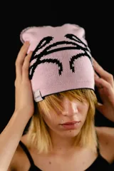 Beanie tejido reversible, con un lado negro y el otro lado rosado claro, ambos con diseño gráfico estampado en contraste.