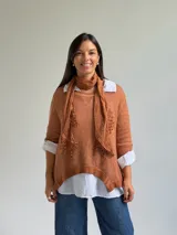 Sweater de punto color naranja con diseño asimétrico, que incluye una bufanda a juego con detalles bordados y una camisa blanca de base integrada.