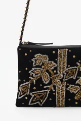 Cartera tipo bandolera de terciopelo negro con bordados artesanales en pedrería dorada y plateada. Cuenta con una correa larga decorada con cuentas y borlas en los extremos, cierre superior y forro interior de algodón.