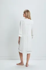 Bata de estar por casa color blanco, confeccionada en tejido suave con caída fluida. Presenta mangas tres cuartos con detalles de transparencias en los puños y el ruedo, bolsillos laterales y un lazo ajustable en la cintura.