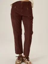 Pantalón de pana color bordó, de corte recto y tiro mid-rise, con diseño de costuras verticales frontales y detalles de tachas metálicas en los bolsillos.