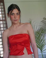 Top strapless color rojo vibrante, con frunces y pliegues que crean un efecto escultural y volumen en la parte delantera. Presenta un corte frontal con abertura central.