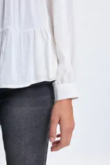 Camisa blanca de corte holgado con diseño de paneles escalonados, cuello clásico, cierre frontal con botones y mangas largas con puños.