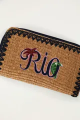 Billetera rectangular color marrón con textura tejida, cierre perimetral con cremallera y bordes decorados con costura en zigzag negra. Cuenta con el texto bordado 'Rio' en tonos violeta y verde con una palmera y un tucán integrados.