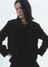 Chaqueta corta de diseño recto, confeccionada en tejido mezcla de lana. Presenta cuello de solapa, cierre frontal de botones y dos bolsillos laterales de ribete. Incluye forro interior y mangas largas.
