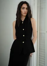 Chaleco negro sin mangas con cuello camisero, cierre frontal con botones dorados y diseño entallado.