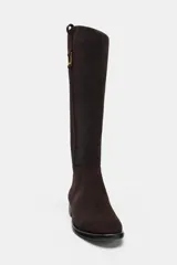 Bota de caña alta confeccionada en serraje, con diseño de estilo hípico. Presenta detalle de pespuntes verticales, tira decorativa con hebilla metálica en la parte superior de la caña y puntera redonda. Cuenta con suela plana de 2,5 cm y sistema de calce tipo pull-on.