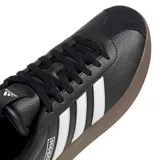 Championes urbanos Adidas modelo VL Court 3.0, color negro con las icónicas tres tiras laterales en blanco y suela de caucho vulcanizado en tono marrón oscuro. Presentan una parte superior de cuero revestido con textura granulada y cierre mediante cordones.