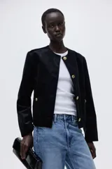 Chaqueta de pana negra con cuello redondo, cierre frontal de botones dorados y dos bolsillos tipo parche en la parte delantera.