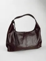 Cartera estilo hobo color chocolate, confeccionada en eco cuero con textura granulada. Presenta una correa ancha fija con detalles de tachas metálicas y un colgante de borla lateral. Incluye cierre superior y herrajes plateados.