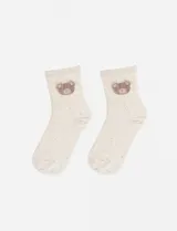 Medias de caña media en color crema con motas de colores y bordado de un pequeño oso en la parte superior.