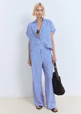 Camisa celeste con rayas verticales blancas, de corte recto, cuello camisero y mangas cortas murciélago. Cierre frontal con dos botones.