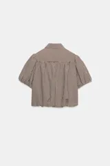 Camisa corta de cuello solapa y manga corta abullonada acabada en elástico, color verde con estampado de cuadros vichy. Cuenta con un bolsillo de plastrón en el delantero, bajo con elástico y cierre frontal con botones.