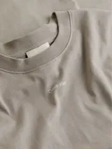Remera gris de algodón regenerativo, corte slim, cuello redondo y manga larga. Logo pequeño de Calvin Klein debajo del cuello.