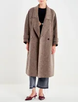 Tapado largo de paño grueso color marrón topo, con cuello solapa ancho y cierre cruzado de doble botonadura con botones oscuros. Presenta mangas largas con puños doblados.