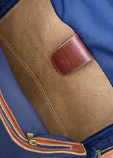 Mochila de cuero negro, con forro interior de lino y herrajes de bronce. Presenta un bolsillo frontal con cierre y un parche de cuero marrón con logo grabado.