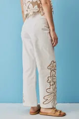 Pantalón negro de tiro alto y corte recto, confeccionado con detalles de bordados florales calados en la parte inferior de las piernas.