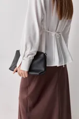 Camisa blanca de manga larga con textura suave y caída liviana, cuello camisero, puños anchos y fruncidos sutiles en los hombros.