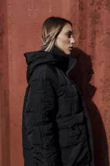 Campera larga acolchonada color marrón, con diseño midi, capucha amplia, cierre frontal con cremallera y broches, y bolsillos delanteros con tapa.