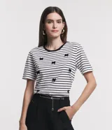 Blusa de media malla a rayas horizontales blancas y negras, con cuello redondo y mangas cortas. Aplicación de moñas negras.