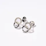 Par de aros colgantes plateados con forma de dos círculos entrelazados, uno liso y otro con pequeños brillantes incrustados.