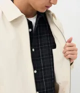 Campera boxy de poliéster color beige, con cuello inglés, cierre frontal de cremallera, mangas largas con elástico en los puños, bolsillos laterales y detalles de recortes.