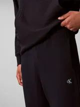 Pantalón de jogging Calvin Klein de felpa color azul marino, con cintura elástica, cordón ajustable, bolsillos laterales y puños elásticos en los tobillos. Cuenta con el monograma CK bordado discretamente en la pierna.