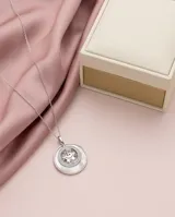 Dije circular de plata 925 con base de nácar y diseño central de figura infantil decorado con circonias multicolor.