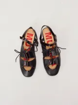 Sandalias planas tipo slingback de cuero negro con costuras en hilo rojo, diseño delantero calado con cordones ajustables y tira trasera con hebilla metálica.