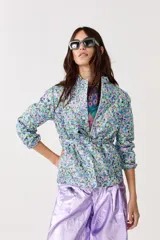 Chaqueta capitoneada con estampado floral y terminación metálica, cuello alto, cierre frontal escondido, cinturón para atar y bolsillos laterales.