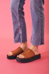 Sandalias tipo chinelas con plataforma plana de goma negra y capellada de cuero color suela con textura.