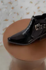 Botineta de cuero charol negro con acabado brillante, diseño de punta fina y taco cuadrado. Presenta un panel elástico lateral y una correa decorativa con hebilla metálica plateada.