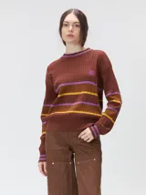 Sweater clásico de punto cable con cuello redondo a la base, mangas largas y fit al cuerpo. De color marrón con franjas horizontales violetas y amarillas, cuenta con el cuello, puños y ruedo acanalados, además de un pequeño logo bordado en el pecho.