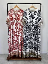 Maxi vestido blanco con estampado paisley en azul marino y detalles en tonos dorados, con cuello en V, mangas amplias y diseño escalonado.