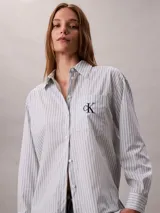 Camisa de Calvin Klein color celeste con patrón de rayas verticales finas y logo 'ck' bordado en el bolsillo frontal. Presenta cuello camisero, cierre frontal con botones y manga larga.