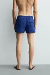 Short de baño azul con cintura elástica ajustable con cordón, bolsillos laterales y ribetes en contraste en los bordes.