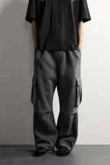 Pantalón jogger de corte relajado confeccionado en tejido de algodón compacto con elasticidad. Presenta cintura elástica ajustable con cordón, bolsillos laterales, bolsillos cargo con solapa en las piernas y detalle de pliegues en las rodillas.