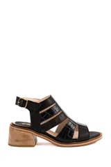 Sandalia de cuero color negro con diseño de tiras anchas, algunas con textura efecto reptil y aberturas laterales. Cuenta con taco cuadrado efecto madera, plataforma baja y tira ajustable en el talón con hebilla metálica.