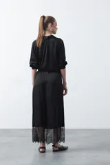 Falda midi negra de caída fluida con cintura elastizada y un amplio detalle de encaje negro en el bajo.