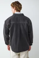 Sobrecamisa de denim en color negro lavado, con cierre frontal de botones metálicos, cuello clásico y un bolsillo de parche en el pecho. Presenta costuras a la vista y puños abotonados.