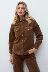 Camisa de pana color tostado, con cuello clásico, cierre frontal con botones metálicos y bolsillos frontales con solapa.