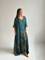 Vestido largo verde petróleo con estampado floral grande en tonos marrones y ocres, de corte amplio, mangas tres cuartos y escote en V.