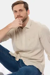 Camisa de manga larga color beige confeccionada en lino, con cuello clásico, cierre frontal con botones, bolsillo en el pecho y logo bordado.