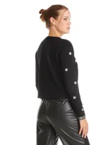 Chaqueta tejida de punto color negro, con cuello redondo y cierre frontal invisible. Presenta un diseño decorado con apliques de strass facetados y perlas en forma de flores y líneas en los bordes.