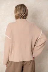 Buzo de punto acanalado vertical en color blanco, con cuello alto y diseño oversize. Presenta detalles de costuras en color negro que recorren los hombros y las mangas.