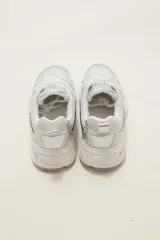 Zapatilla deportiva de estilo urbano en color blanco con detalles metalizados plateados y acentos en negro. Presenta una combinación de malla transpirable y paneles sintéticos, con suela robusta y cordones al tono.