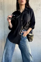 Camisa negra de corte oversize, con cuello clásico, manga larga y bolsillo en el pecho.