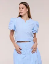 Blusa celeste a rayas blancas de calce recto con textura gofrada, cuello redondo con escote en V y mangas cortas abullonadas con elástico en los puños.
